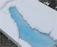 The lucite ice river takes shape as borders are glued around it.  On a completely temporary railroad or village setting you could use pebbles or some such to hide the edges and give the river shape. Click for bigger photo.